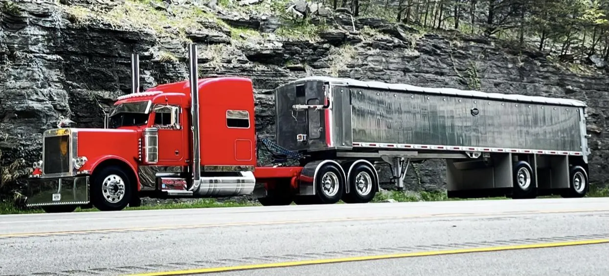 Mullins Trucking grain trailer passing a Kentucky rock cut
