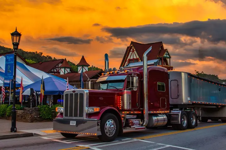 Maroon Mullins Trucking Peterbilt with a tarped trailer on a village street at sunset